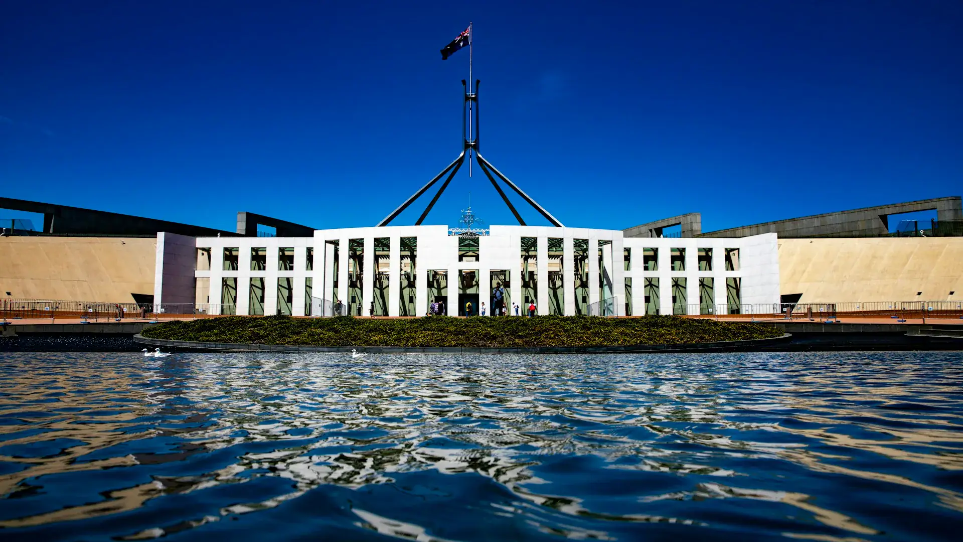 Parlamentshuset i Canberra med australiska flaggan på masten över dammen Parlamentshuset i Canberra med australiska flaggan på masten över dammen